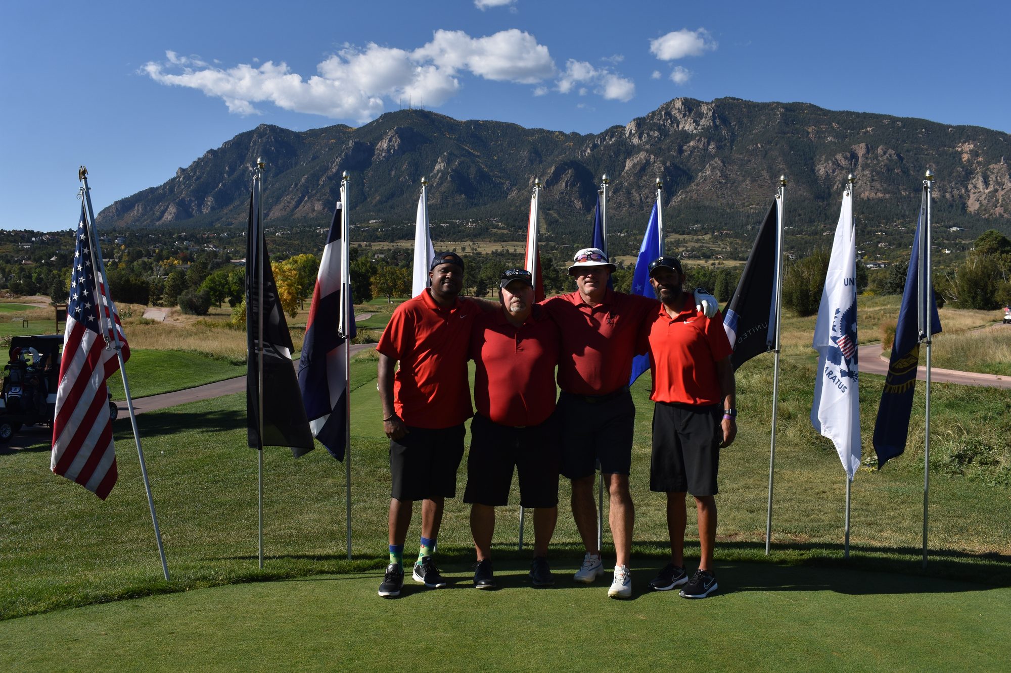 A foursome on the tee box in front of the service flags and Cheyenne Mountain